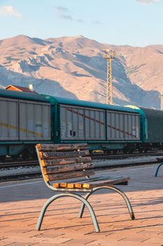 An empty bench at a scenic railway station with mountains in the background.