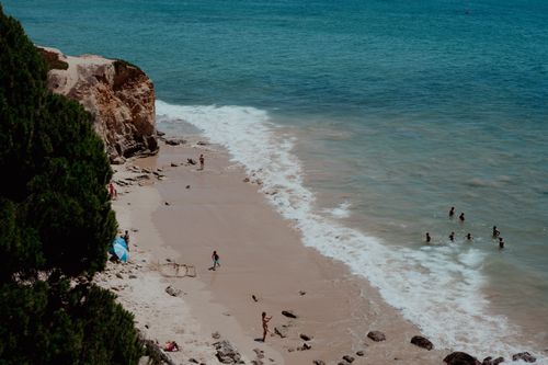 Free High-angle shot of a vibrant beach day with people enjoying the sea and sun near a rocky cliff. Stock Photo