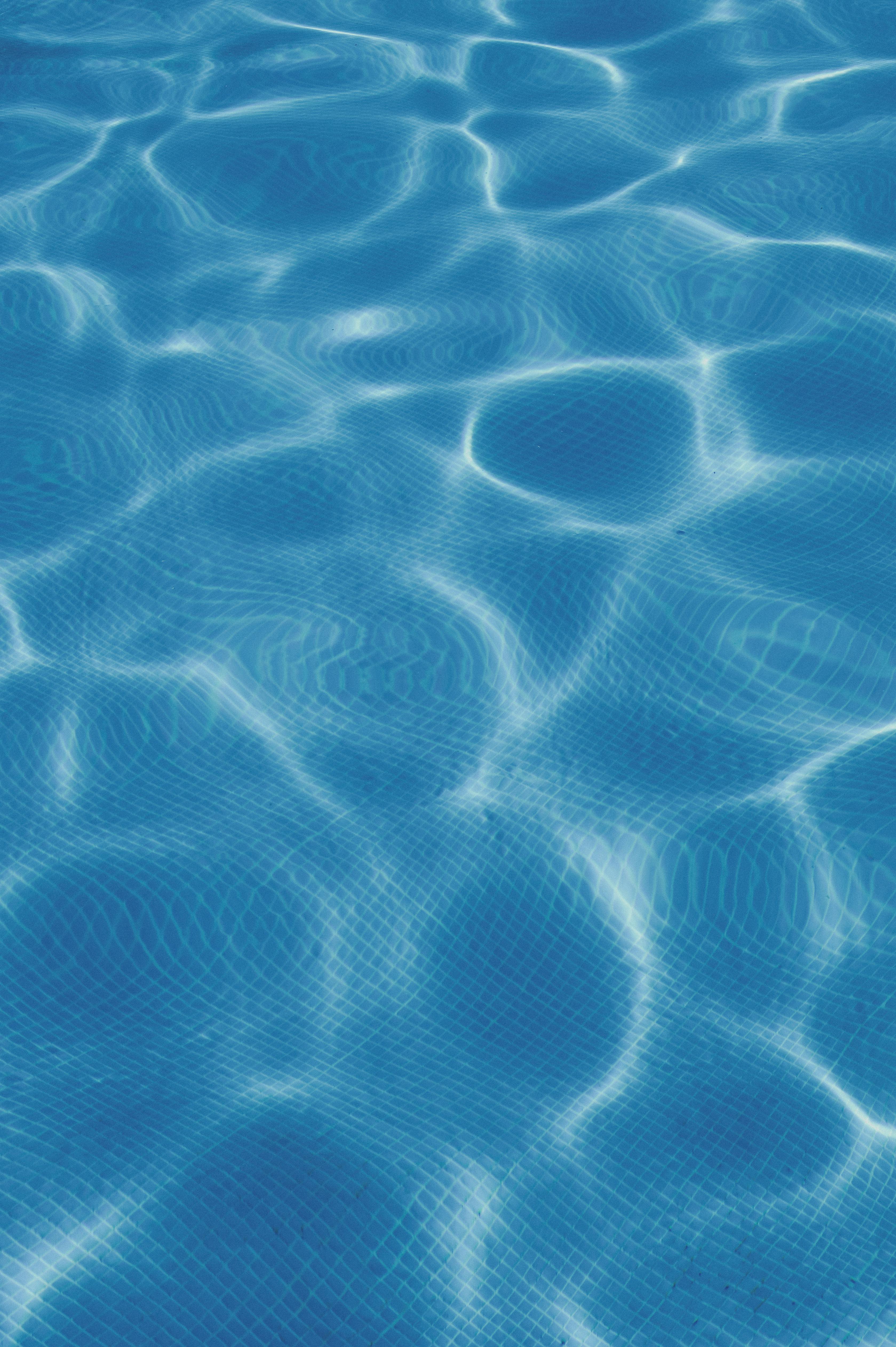 Calm blue swimming pool water with clear reflection and ripples in sunlight.