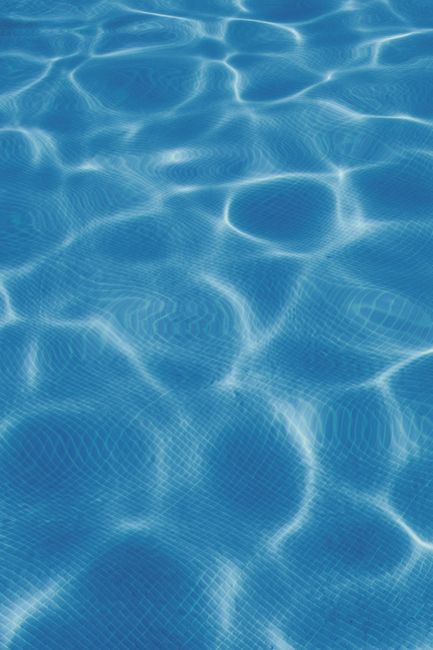 Calm blue swimming pool water with clear reflection and ripples in sunlight.