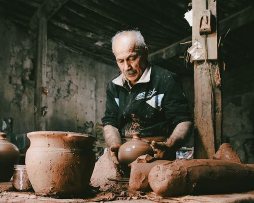 Free Senior man skillfully shaping clay pots in a rustic pottery workshop, showcasing traditional craftsmanship. Stock Photo