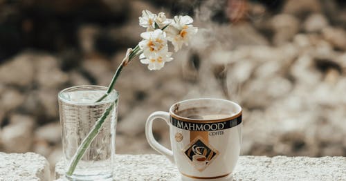 Free White-and-yellow Flowers in Clear Glass Beside White and Black Mahmood Ceramic Cup Stock Photo