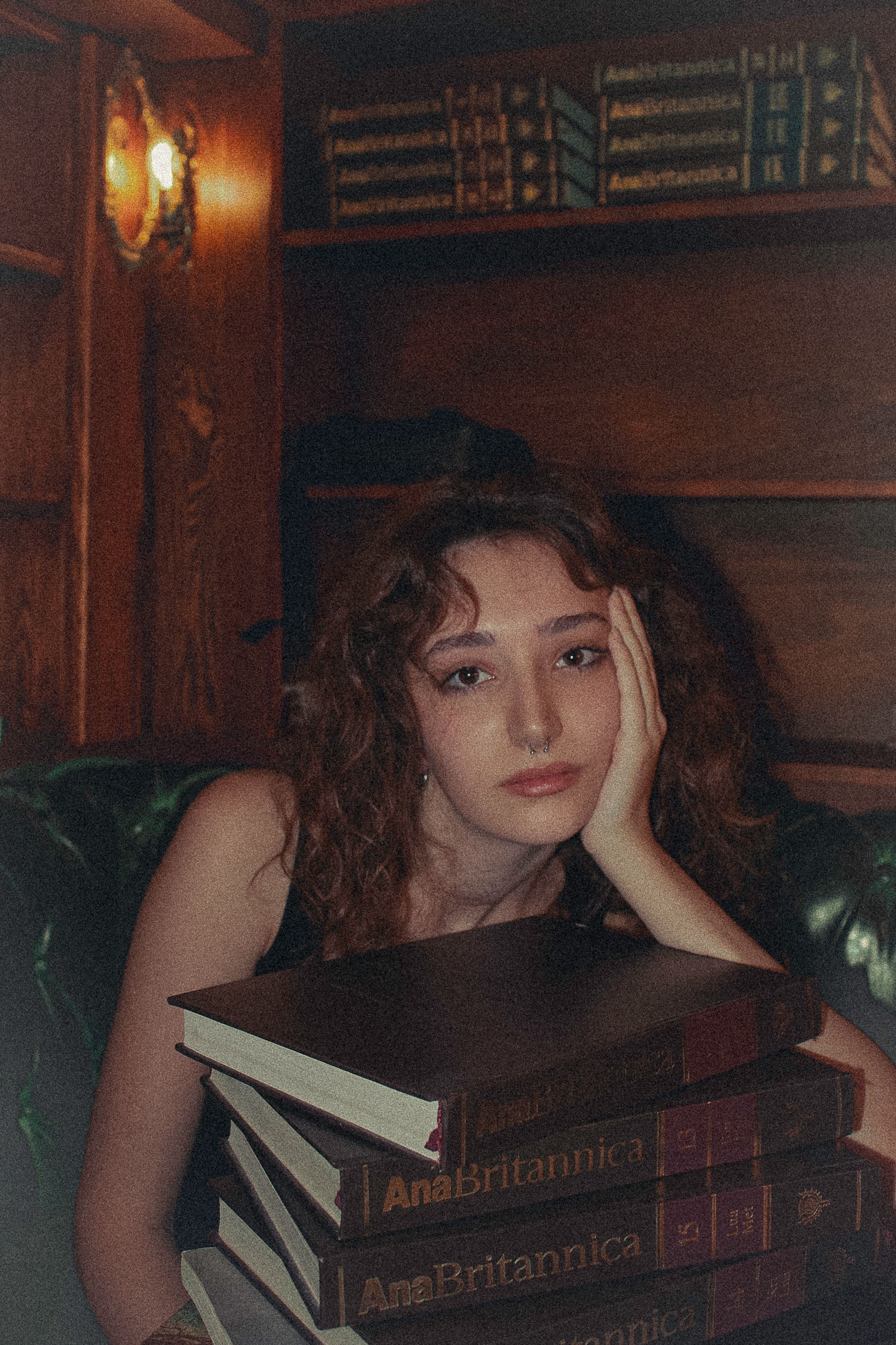 Portrait of a young woman resting in a library with a stack of books.