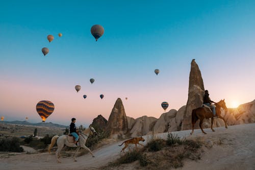 People Horseback Riding with Dog on Trail Overlooking Flying Hot Air Balloons
