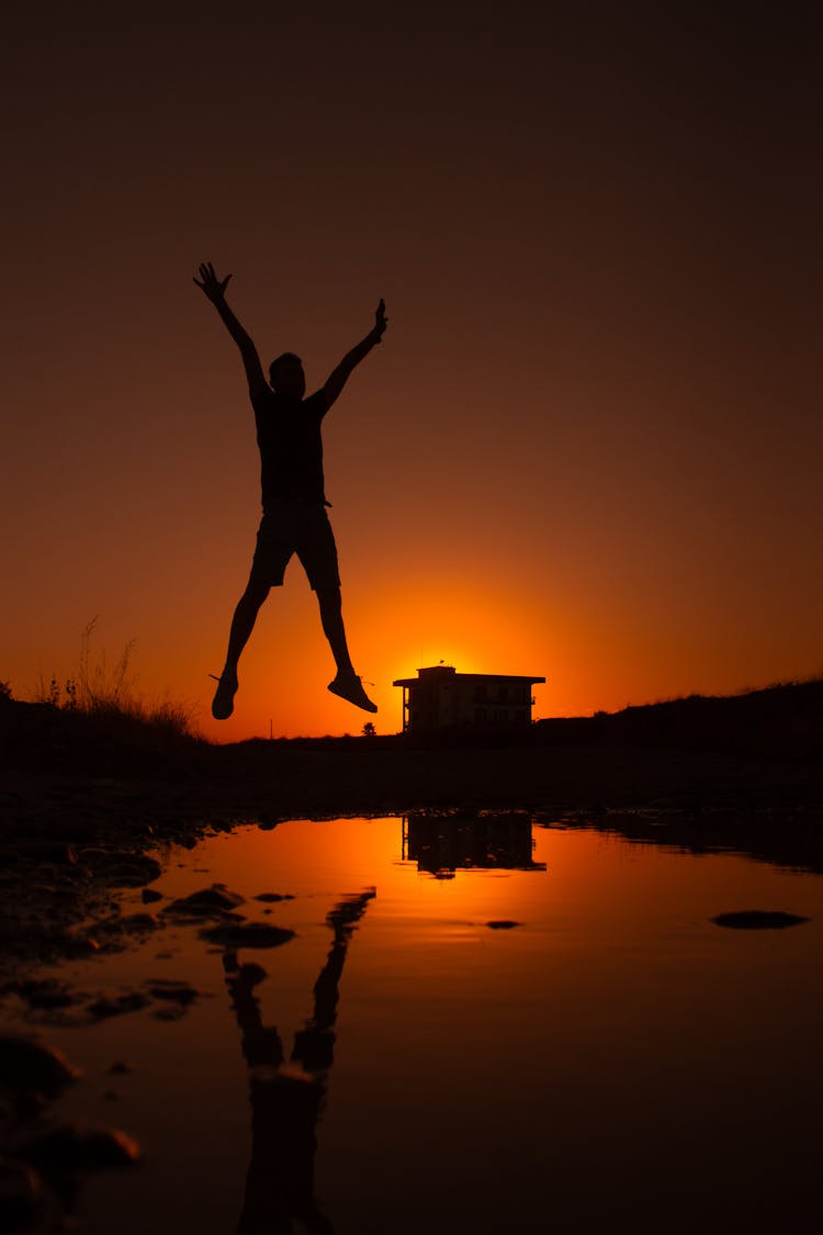 Silhouette Of Person Jumping Into Lake At Sunset