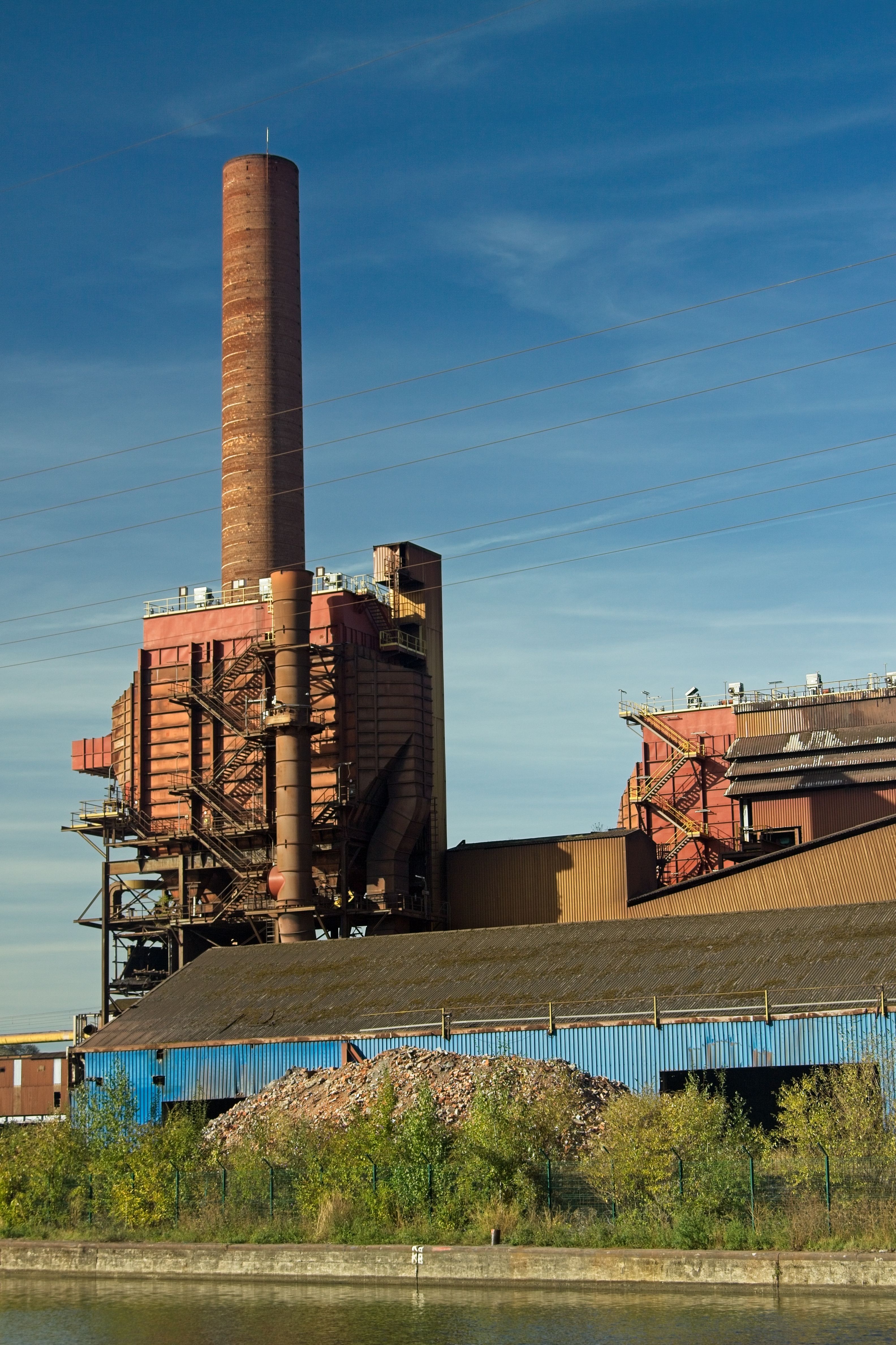 An industrial factory with a prominent tall chimney under clear blue skies.