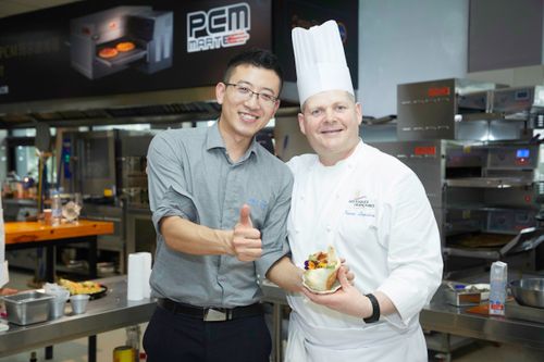Free A smiling chef and customer in a commercial kitchen enjoying delicious food. Stock Photo