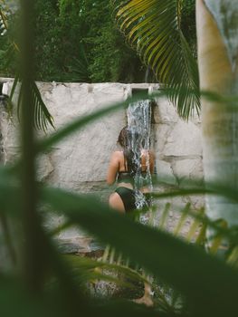 A woman relaxes under a waterfall shower surrounded by lush greenery in Cusco, Perú.