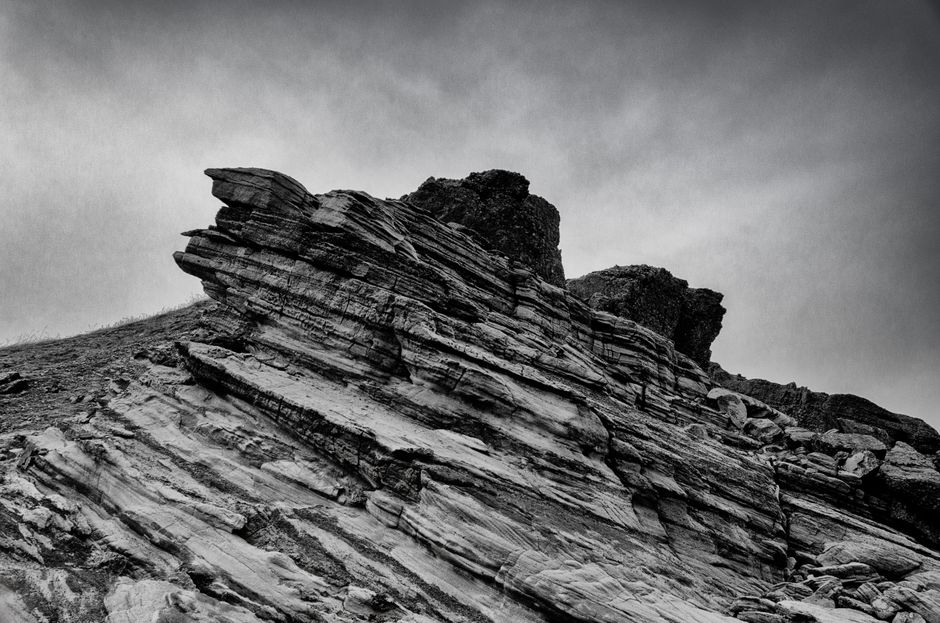 A striking black and white photo of a rugged, dramatic rocky cliff formation under a moody sky.