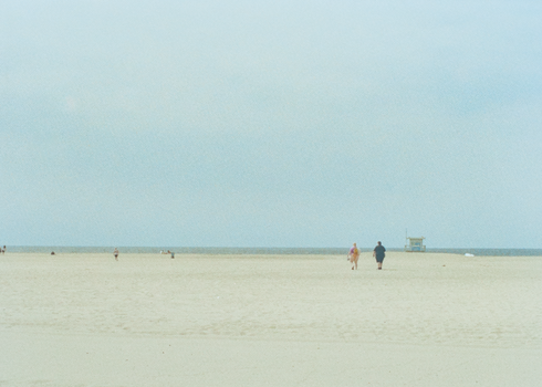 Wide sandy beach with tourists walking near the ocean under a clear sky.