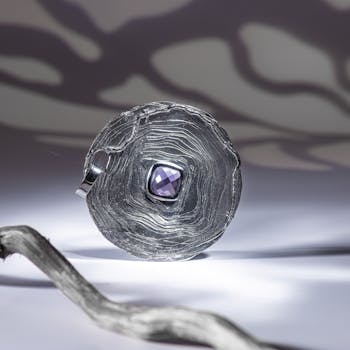 Close-up shot of artistic silver jewelry with purple gemstone accent and elegant shadows.