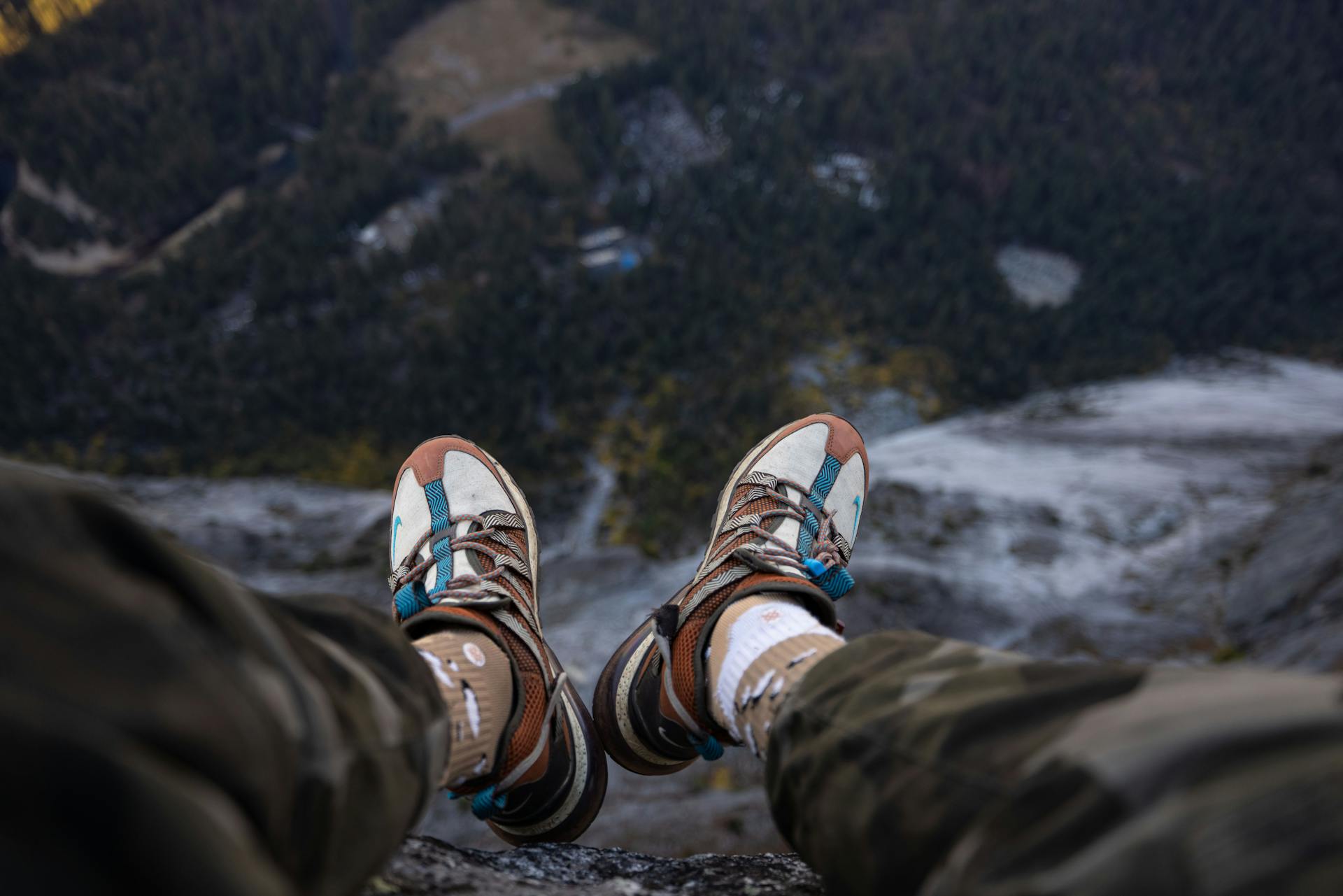 Hiker's legs dangling over a steep cliff edge, showcasing mountain views.