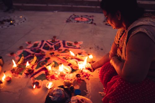 Free A woman celebrates a traditional Indian festival with rangoli and candles lighting the night. Stock Photo