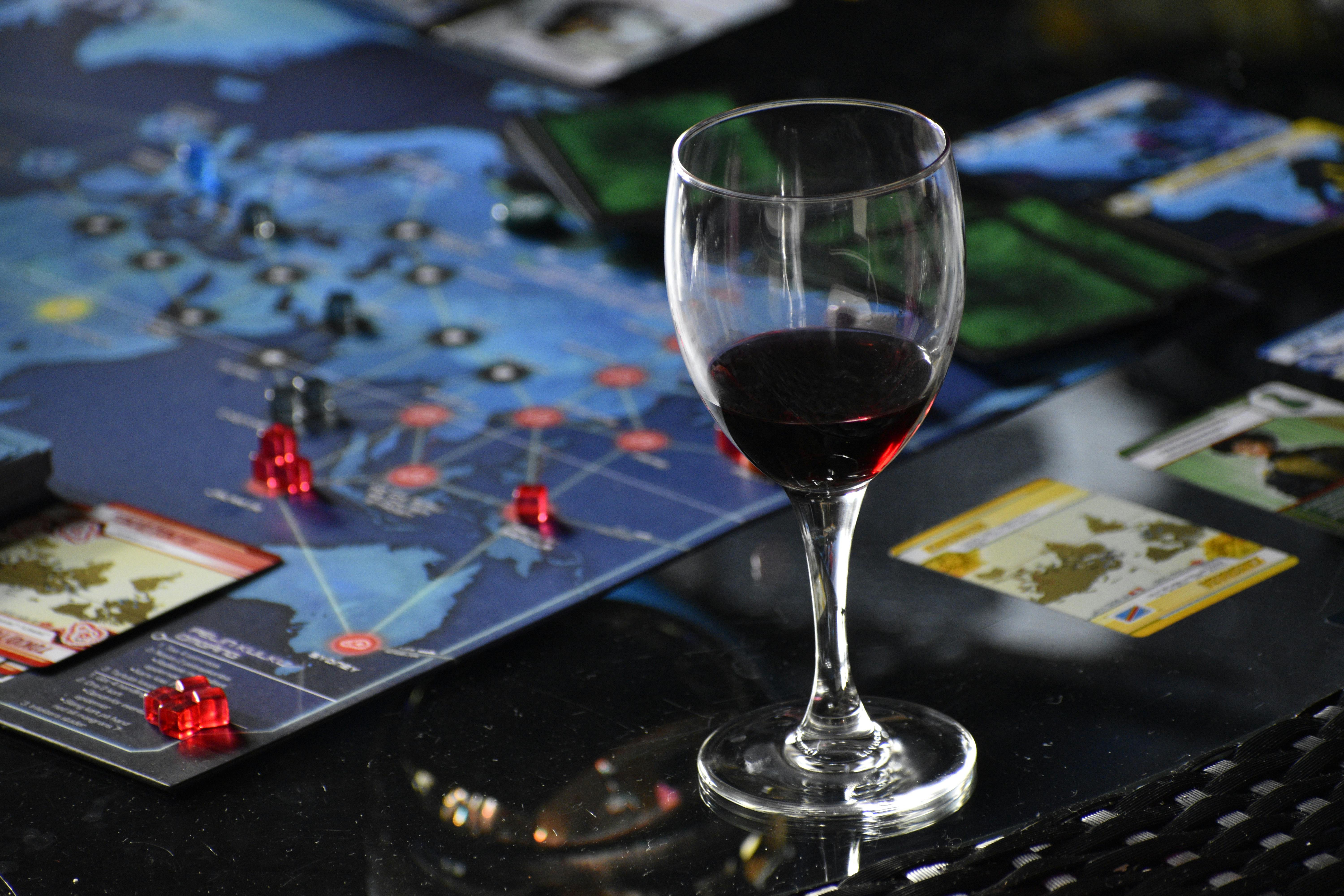 Elegant glass of red wine beside a strategic board game setup on a table.