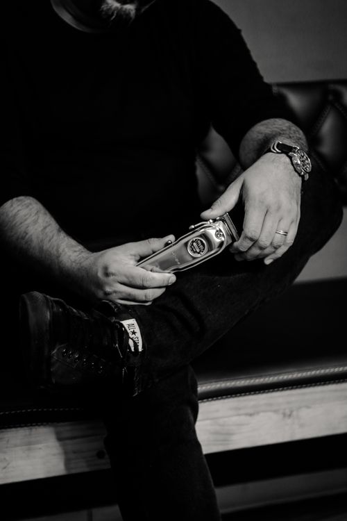 Free A man sitting on a bench, holding a cordless clipper in a barbershop setting. Stock Photo