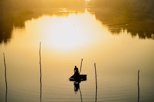 Silhouette of a Fisherman Standing on a Raft on a River at Sunrise
