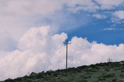 Free A scenic view of power lines against a vibrant blue sky with fluffy clouds over a rural hillside. Stock Photo
