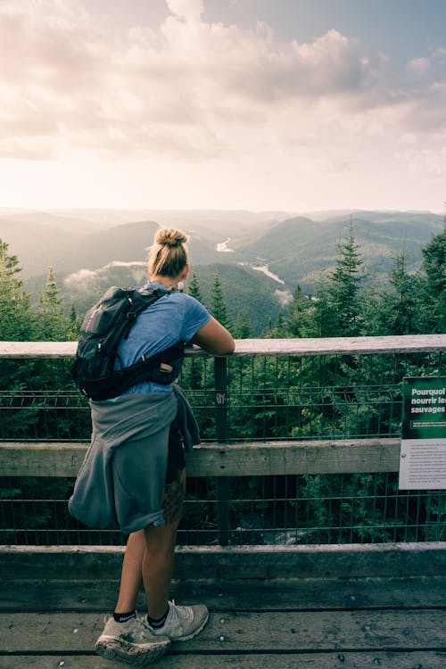 Blonde Man with Backpack Standing by Railing over Forest