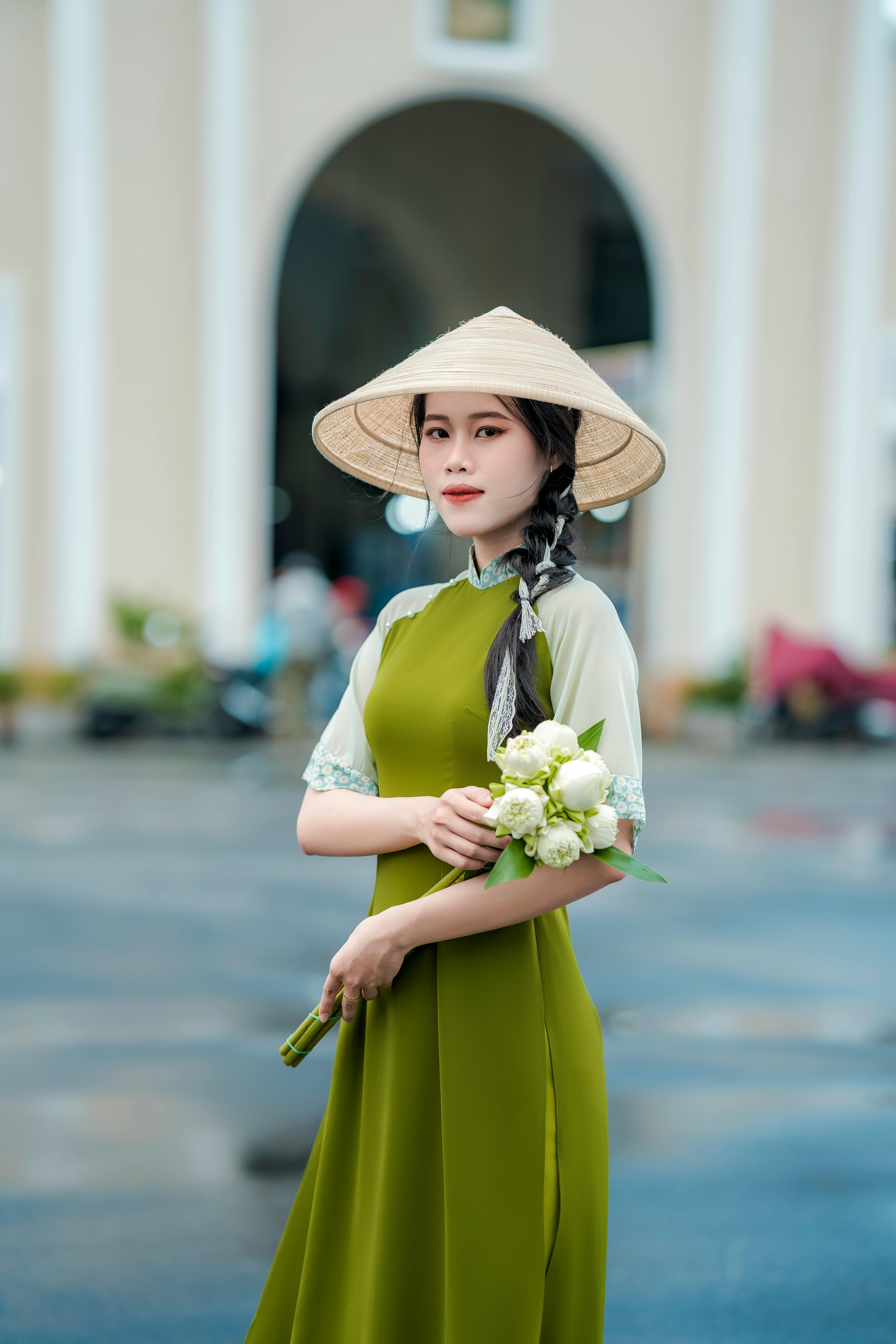 Asian woman in a conical hat and traditional clothing holding flowers in Ho Chi Minh City.