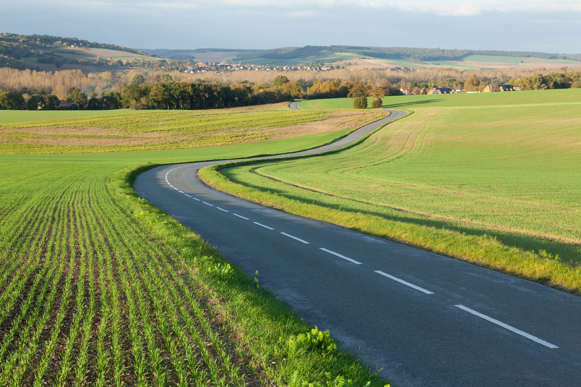 Serene countryside road through green fields in Gommecourt, IDF, France.
