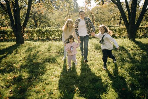 Free A joyful family with two kids playing in a sunlit countryside setting, enjoying a summer day. Stock Photo