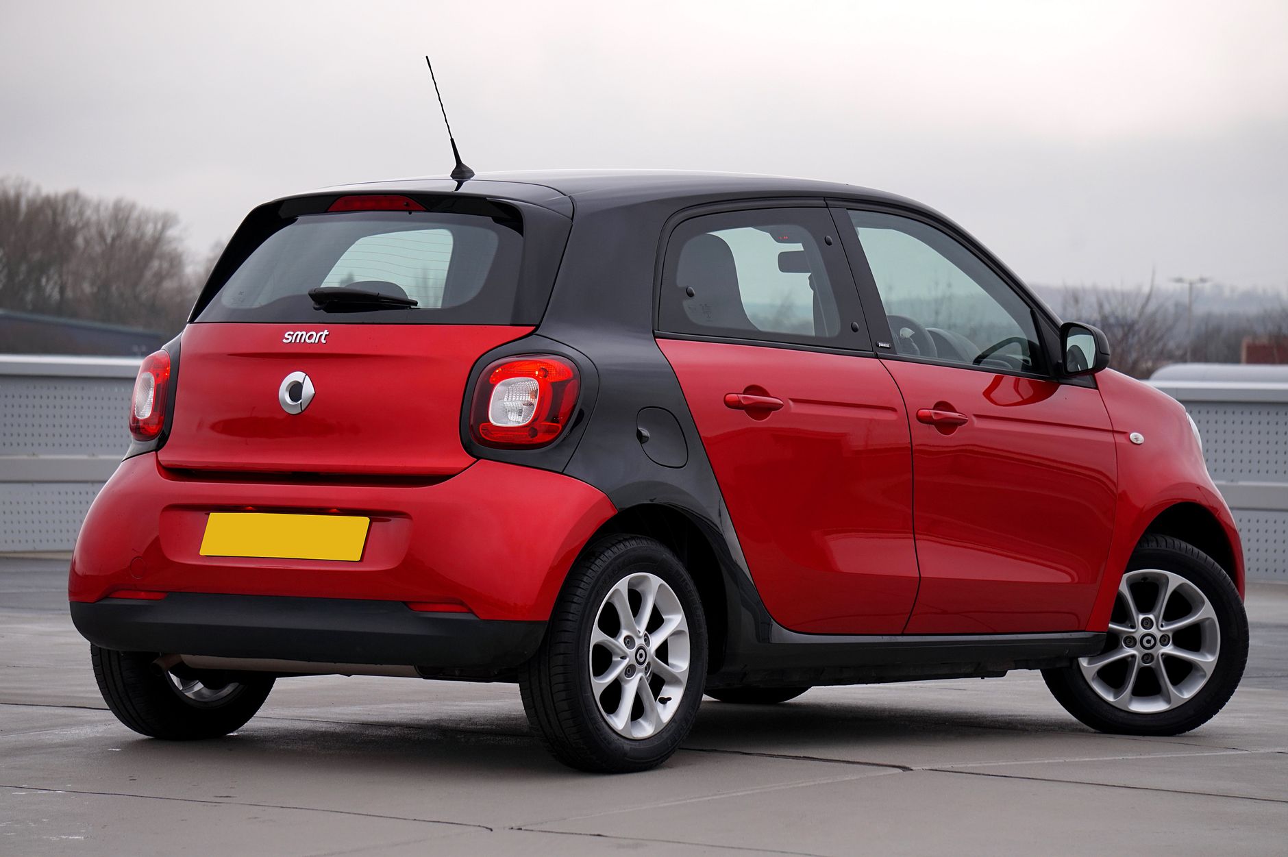 Rear view of a red Smart Forfour parked outdoors on a cloudy day, showcasing sleek design.