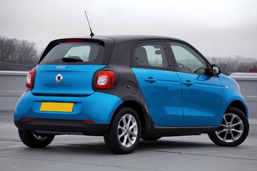 A blue Smart car parked outdoors viewed from the back, highlighting urban mobility.