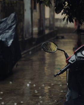 A motor scooter parked in a rainy urban alley, reflecting wet pavement and a moody atmosphere.
