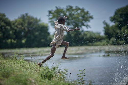 Free Young boy jumps midair into a lake in Zaria, Nigeria, enjoying summer fun outdoors. Stock Photo