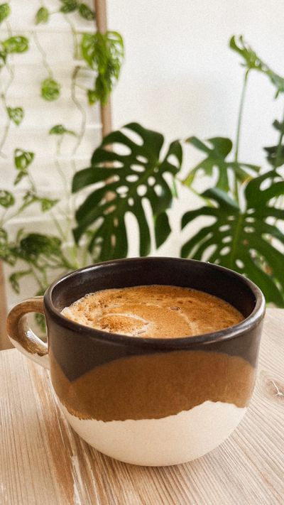 Un cappuccino dans une tasse en céramique devant un grand monstera.