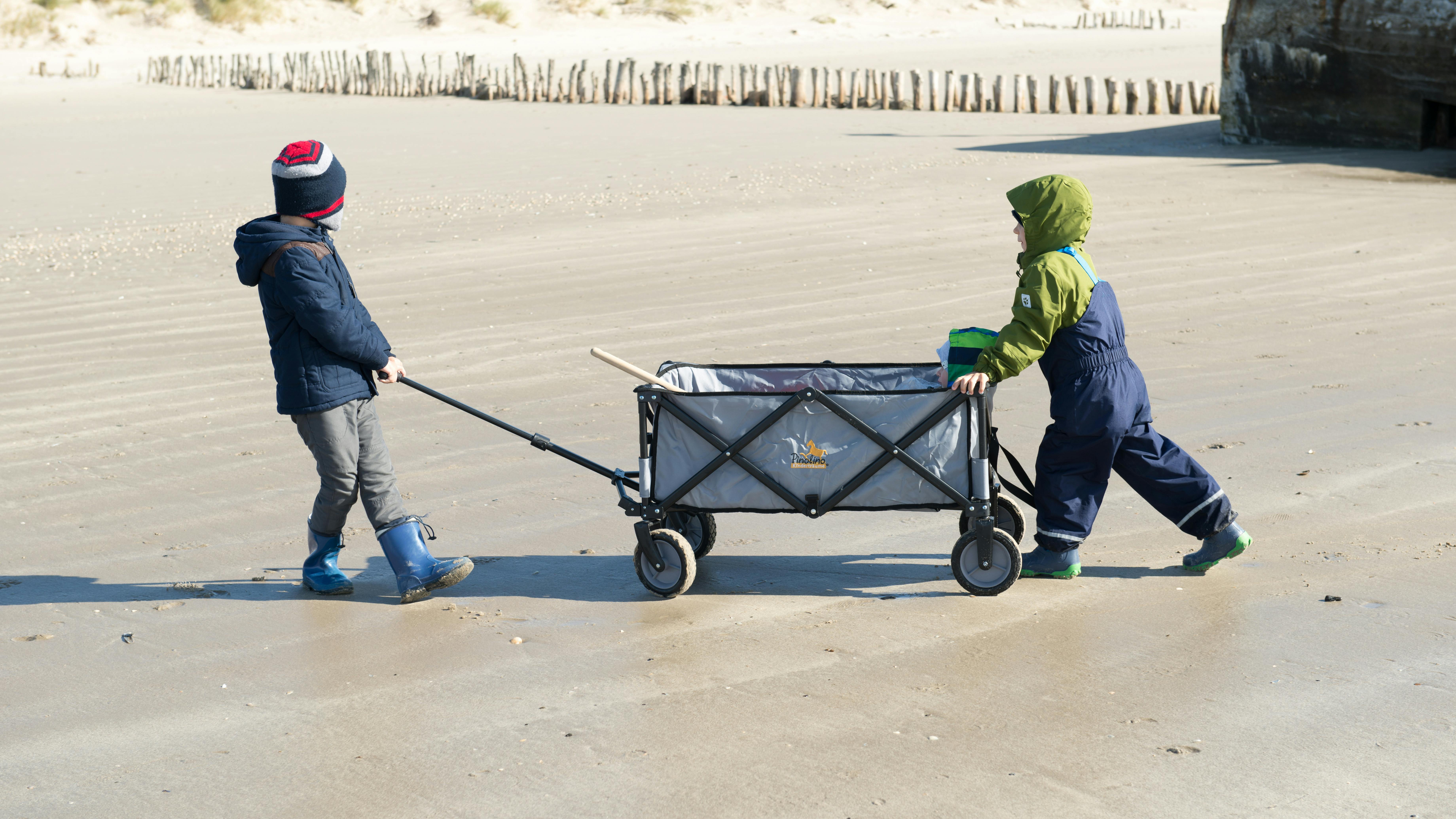 Two children enjoy a sunny day at Esbjerg Beach, Denmark, pulling a cart.