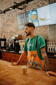 Barista serving iced coffee in a trendy cafe with exposed brick walls and digital menu.
