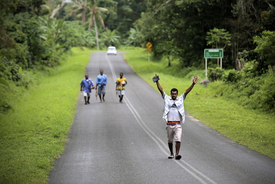 A group of men walk joyfully on a rural road surrounded by vibrant greenery.