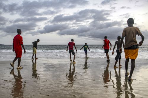 Free Group of boys enjoying a soccer game on the beach at dusk, reflecting their lively spirit. Stock Photo