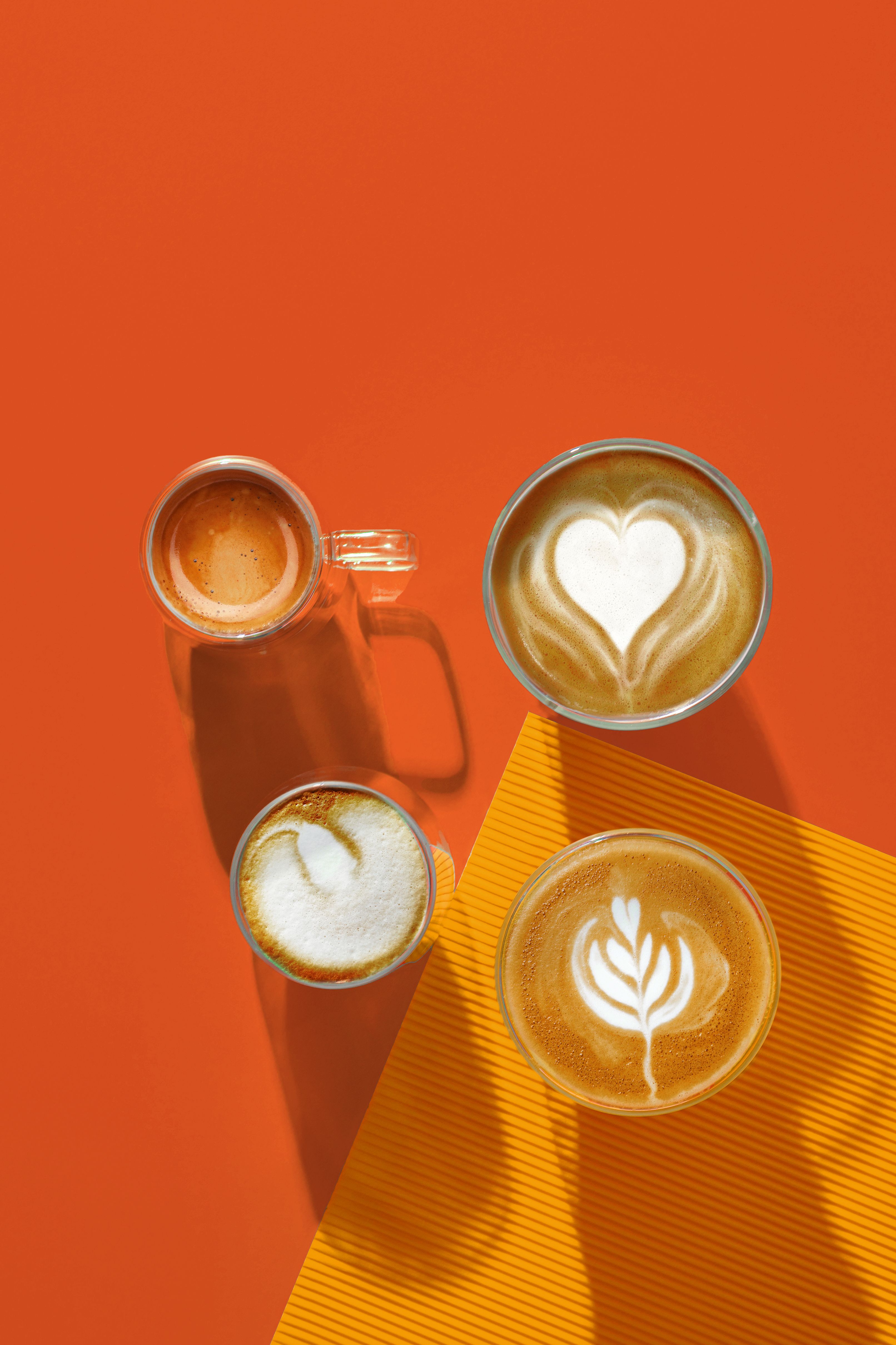 Stylish top view of assorted coffee cups on a bright orange background showcasing latte art designs.
