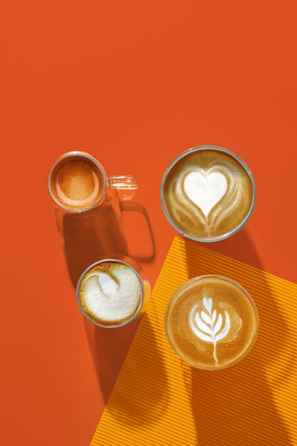 Stylish top view of assorted coffee cups on a bright orange background showcasing latte art designs.