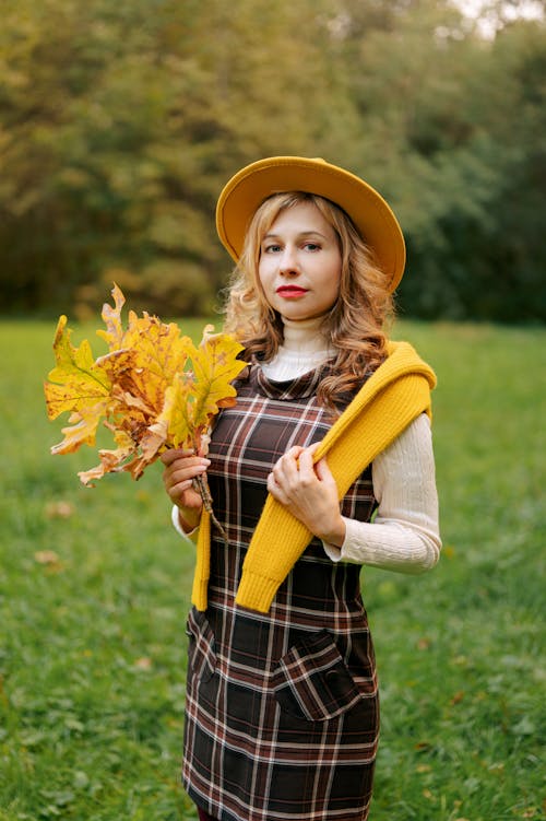 Young Woman in a Checkered Dress with Autumn Leaves in her Hand