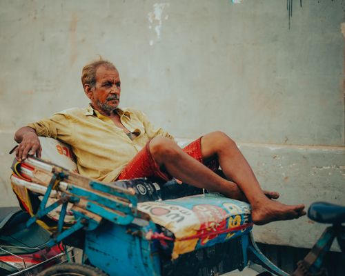 Free Elderly man sitting leisurely on a colorful rickshaw barefoot, captured outdoors. Stock Photo