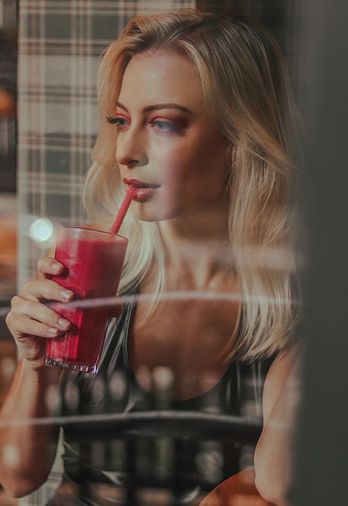 Free A fashionable woman sipping a berry smoothie through a window reflects elegance and healthy lifestyle. Stock Photo