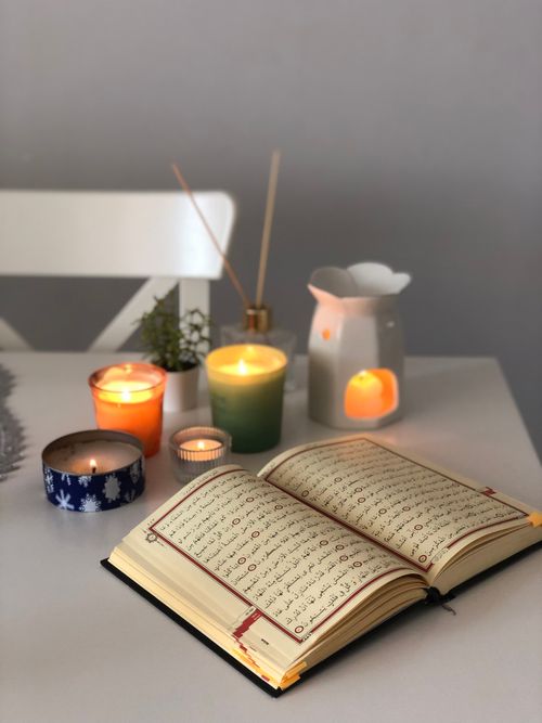 Free An open book surrounded by lit candles on a cozy table setting, creating a warm atmosphere. Stock Photo