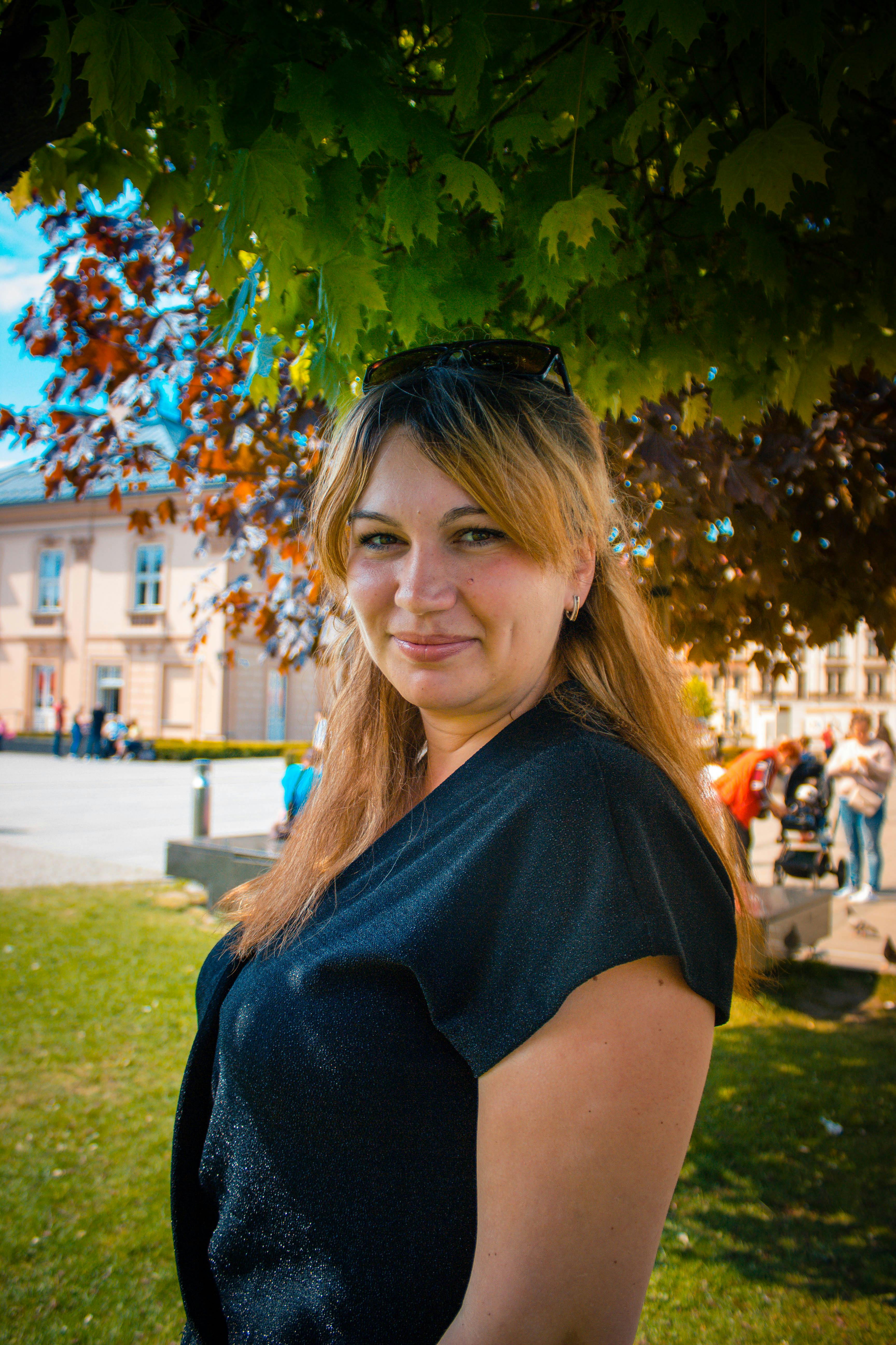 A woman smiles under tree shade in Krakow, perfect for lifestyle themes.