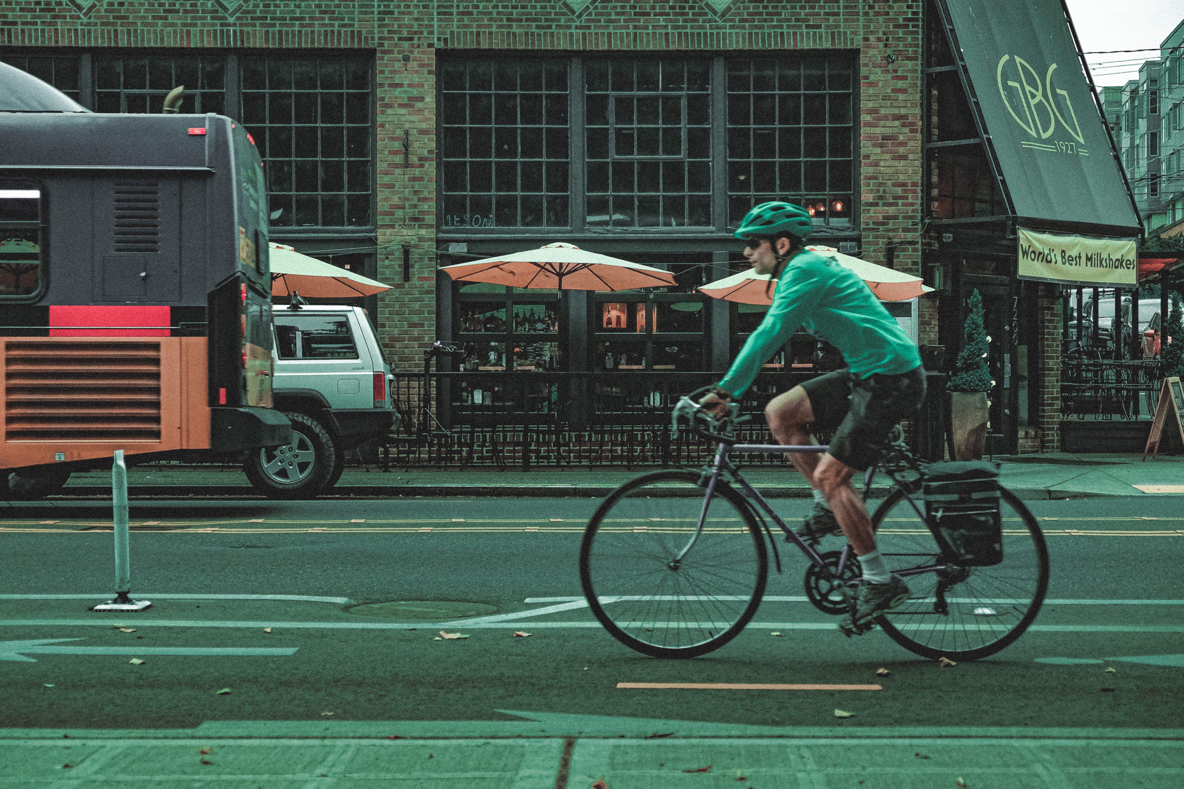 Cyclist in green on a Seattle street with a restaurant backdrop and urban traffic.