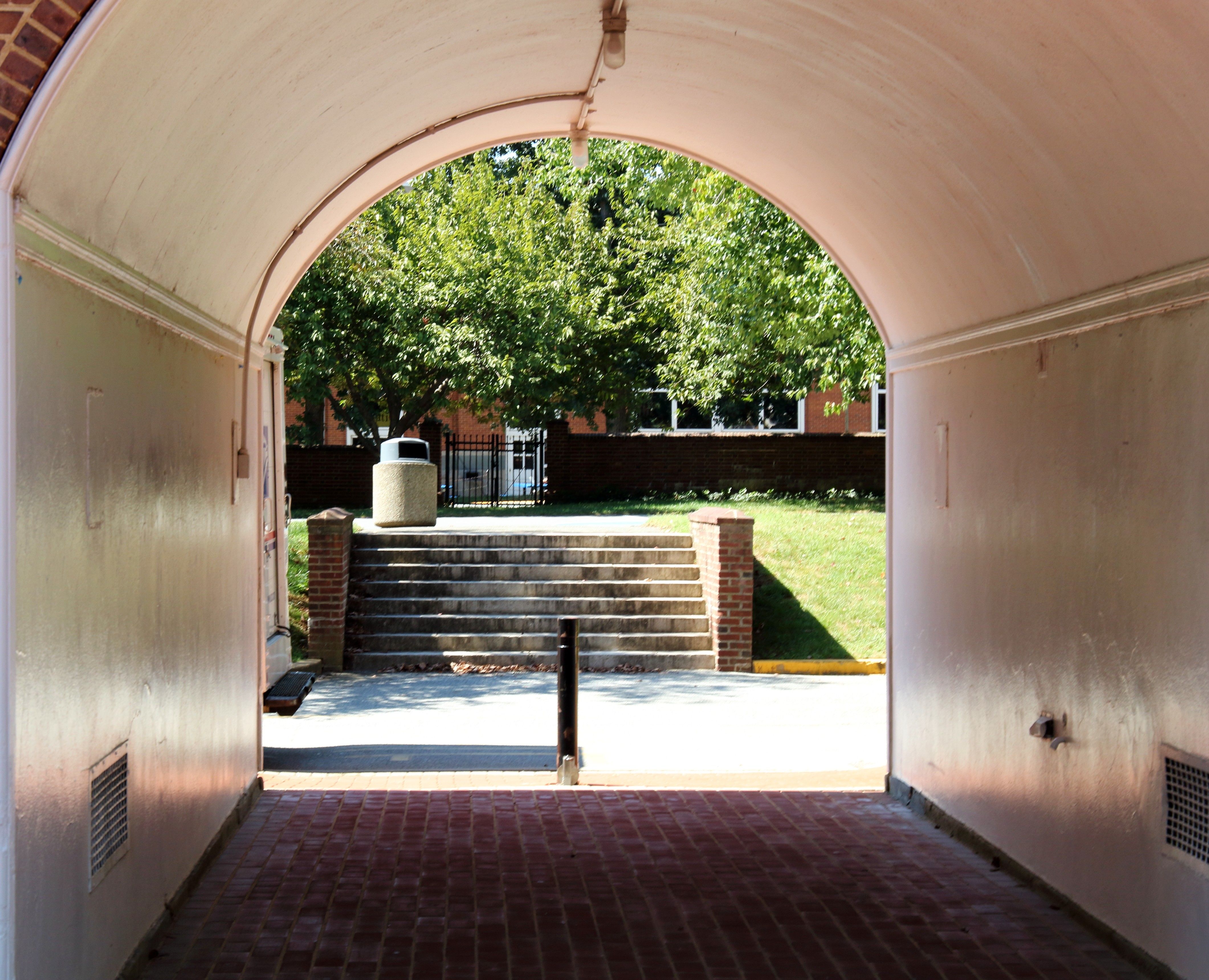 View through an archway to a sunlit area with steps, trees, and buildings in Newark, DE.