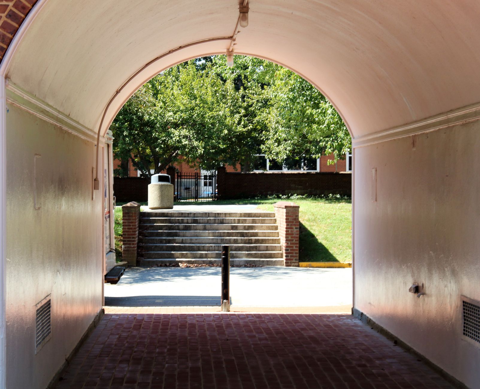 View through an archway to a sunlit area with steps, trees, and buildings in Newark, DE.