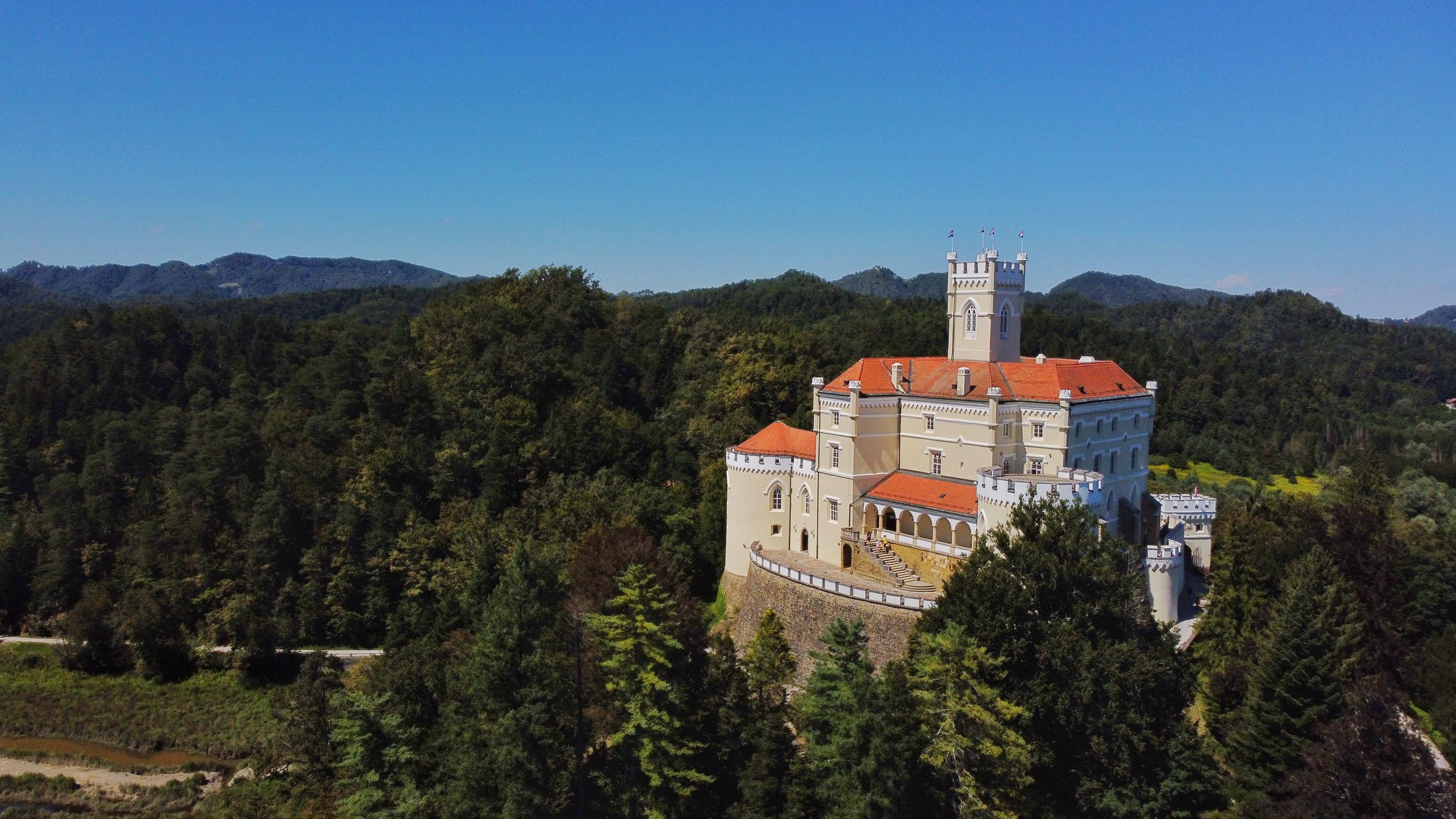 Hluboká Castle at golden hour with Neo-Gothic spires, South Bohemian countryside, and Vltava River views glowing in warm morning light