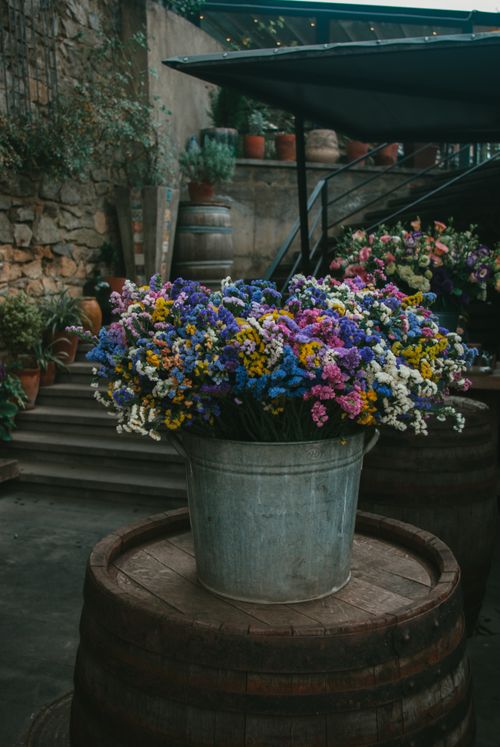 Free Vibrant wildflowers arranged in a metal bucket on a wooden barrel, showcasing rustic outdoor decor. Stock Photo