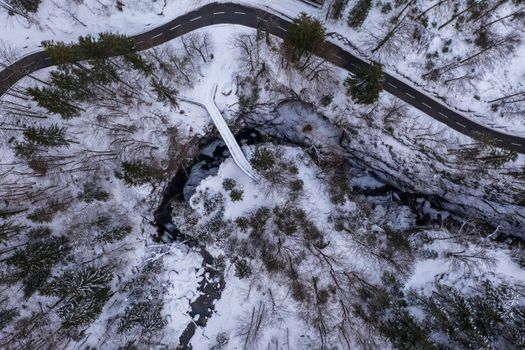 Aerial view of a snowy Riedern forest with winding road and trees in Switzerland.