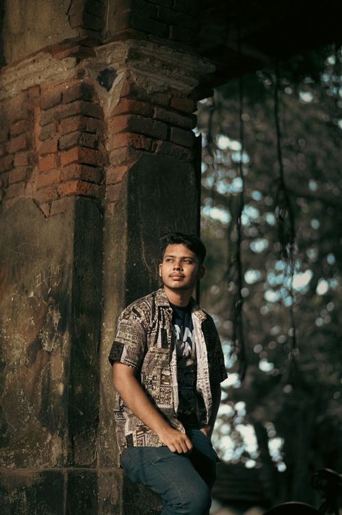 Free Portrait of a young man leaning against an old brick structure, with soft lighting and a relaxed atmosphere. Stock Photo