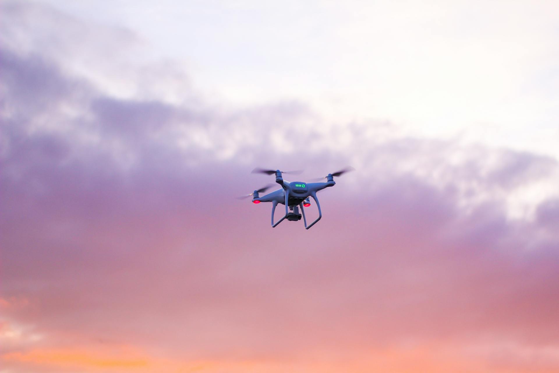 A modern drone flying in the sky with colorful sunset clouds, showcasing advanced aerial technology.