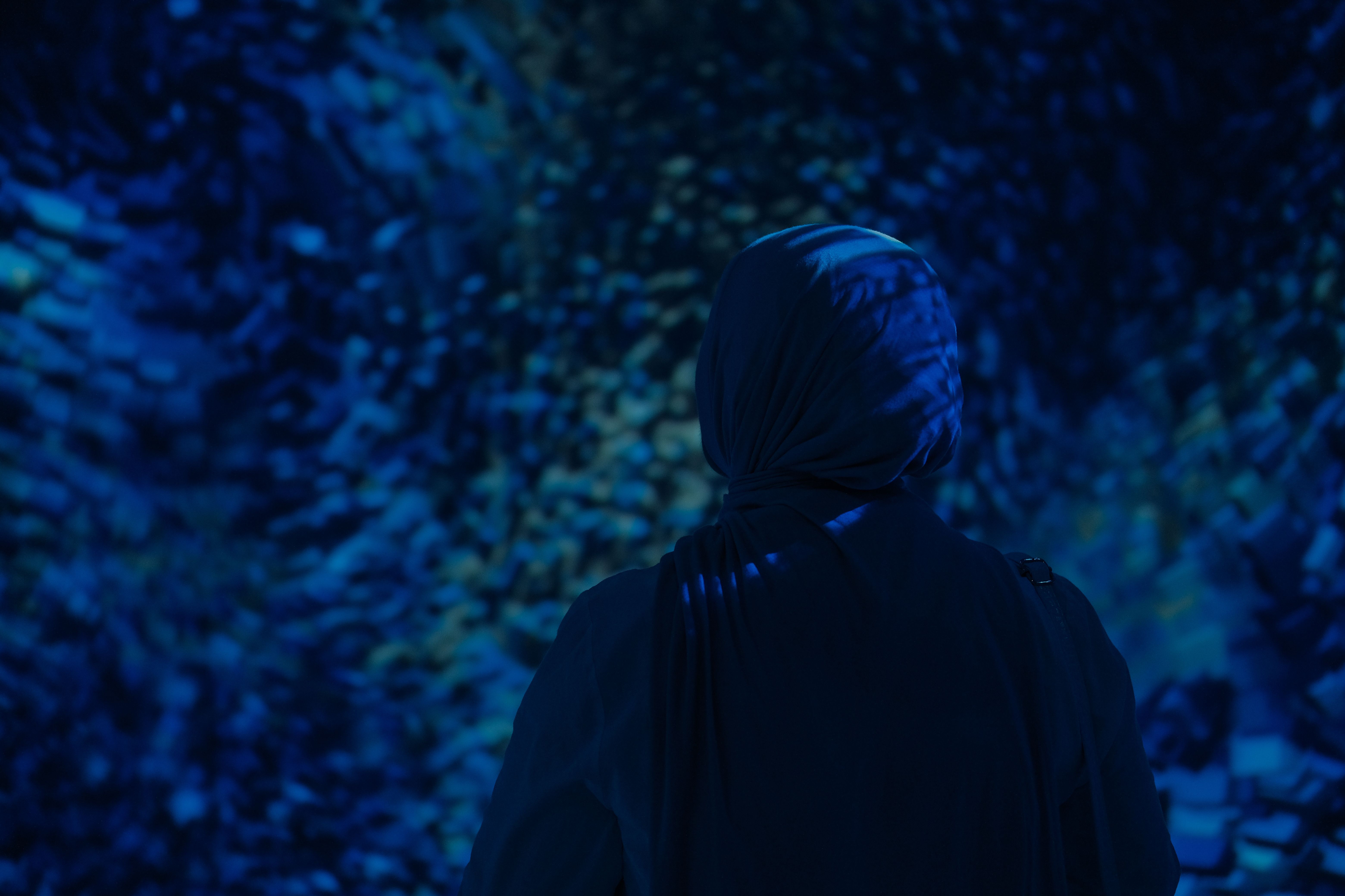 Silhouetted woman in hijab stands against a dark, aquatic-themed background creating a serene and re